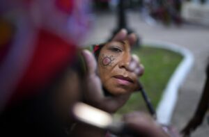 A Maka Indigenous woman puts on make-up before protesting for the recovery of ancestral lands in Asuncion, Paraguay, Wednesday, Feb. 28, 2024. Leader Mateo Martinez has denounced that the Paraguayan state has built a bridge on their land in El Chaco's Bartolome de las Casas, Presidente Hayes department. (AP Photo/Jorge Saenz)