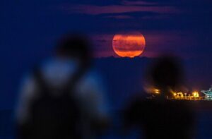 TOPSHOT - People watch the April's full moonset, also known as the "Pink Moon", rising behind the clouds in Singapore on April 24, 2024. (Photo by Roslan RAHMAN / AFP) (Photo by ROSLAN RAHMAN/AFP via Getty Images)